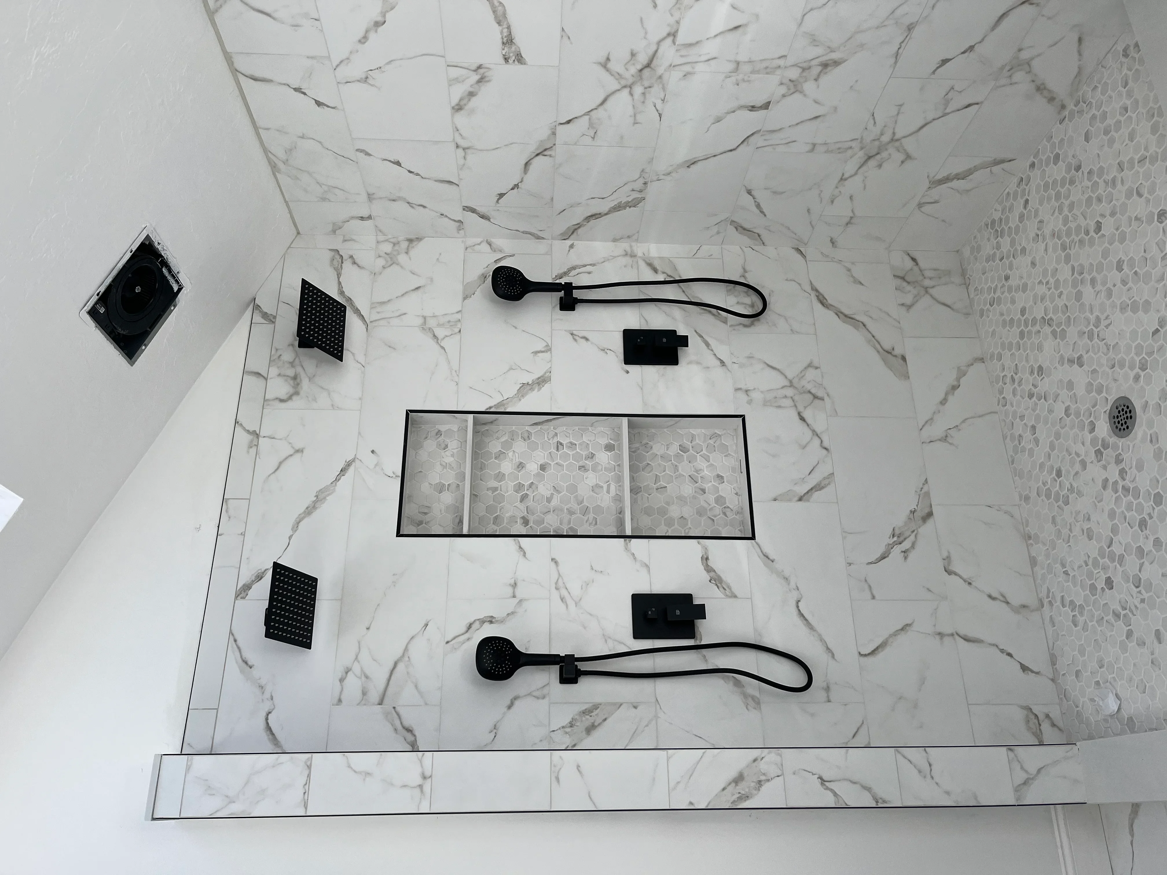 Overhead view of marble shower with dual rainfall heads, body sprays, and glass enclosure